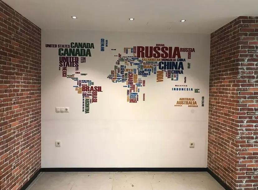 Buğra Dizayn uygulaması: tuğla kolonlar arasındaki duvarda, ülke isimlerinden oluşan tipografik dünya haritası duvar kağıdı